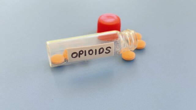 Opioids word label note on medicine bottle with scattered pills isolated on table background with copy space. Powerful analgesic drug medication to manage or relieve severe pain.