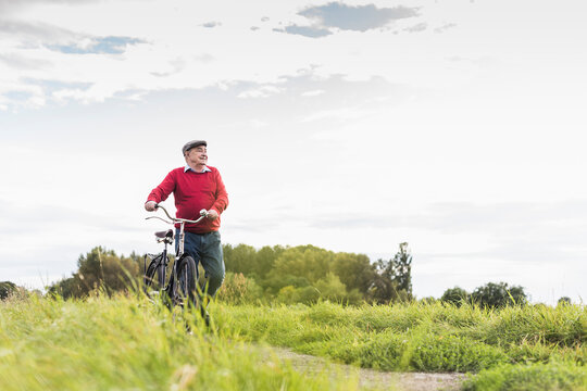 Senior man pushing bicycle in rural landscape
