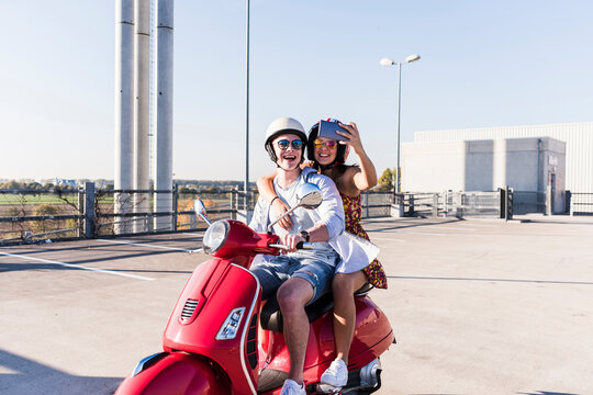 Happy young couple taking a selfie on motor scooter on parking level