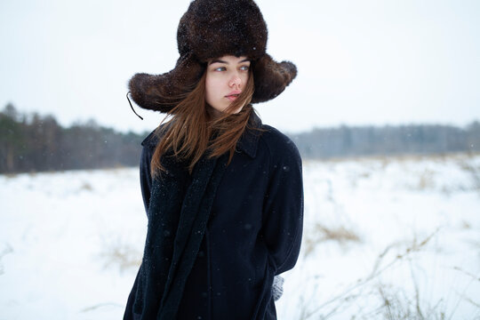 Woman in fur ushanka hat and coat outdoors in snowy winter landscape