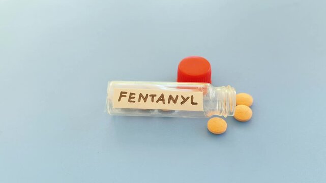 Fentanyl word label note on medicine bottle with scattered drugs or pills isolated on table background with copy space. Powerful analgesic drug medication to manage or relieve severe pain.