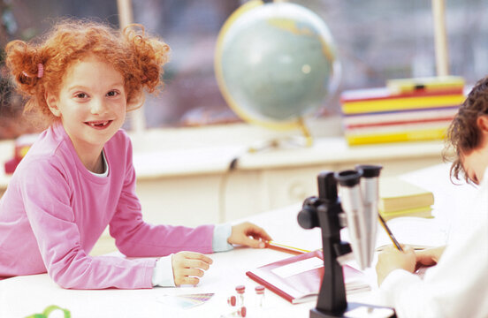Boy and girl (6-9) sitting by microscope, smiling