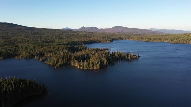 4K aerial drone footage of Summit Lake near Diamond Peak Wilderness, Oregon, USA, at sunset on a clear late summer evening, surrounded by dense evergreen forest in the Cascade Mountains