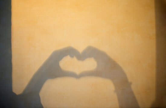 Hands forming heart shape shadow on textured background, soft lighting creates a warm atmosphere, ideal for romantic or affectionate themes in photography