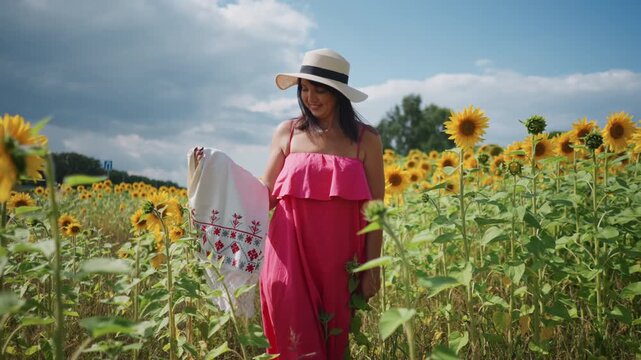 Woman in pink dress and hat stands among sunflowers holding patterned cloth with clear blue sky and green field background sunflower pattern summer outdoor
