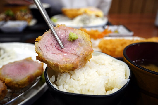 Tender and juicy pink medium rare pork tenderloin tonkatsu held with chopsticks close up