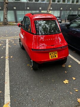 Red Microlino electric microcar parked on an urban street in London, eco-friendly EV e-mobility and compact city transportation concept.