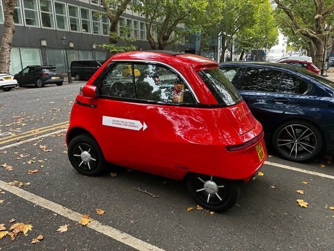 Red Microlino electric microcar parked on an urban street in London, eco-friendly EV e-mobility and compact city transportation concept.