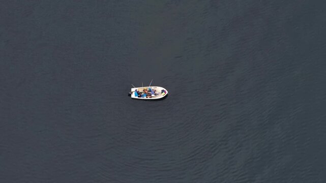 Aerial view of a small white boat with people fishing in the dark water of a fjord in Valldal, More og Romsdal, Norway.