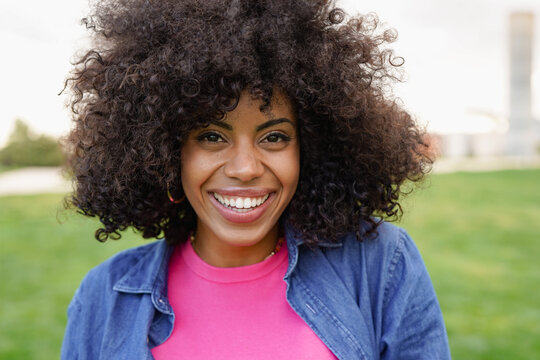Happy young african woman smiling on camera at city park - Portrait of beautiful woman with afro hair outdoor - Lifestyle and happiness concept