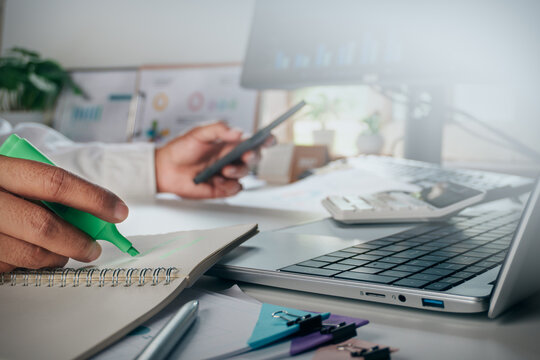 Business professionals highlighting important information and reviewing financial documents with laptop, smartphone, calculator and notebooks, data analysis, accounting, planning and decision making.