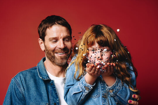 Playful young girl with her father blowing confetti in a joyful studio portrait
