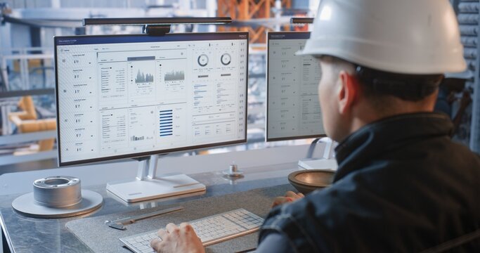 Inside Glass Office, an Engineer Works at Dual Screens Showing Car Parts While Automated Conveyor Robots Assemble Cars in Plant. Smart Robotics Optimize Industry 4.0 Workflow. AI Manufacturing.