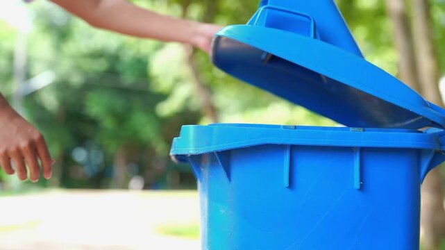 Close-up of hand dropping plastic cup into blue recycling bin outdoors, person recycling waste in garden, environmental sustainability and eco-friendly concept