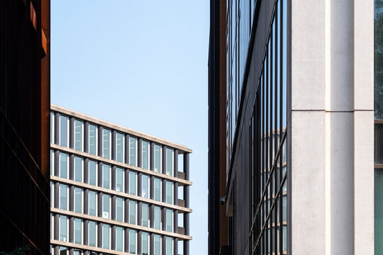 Modern buildings frame a narrow view of blue sky in an urban architecture scene where contrasting facades face each other across the opening