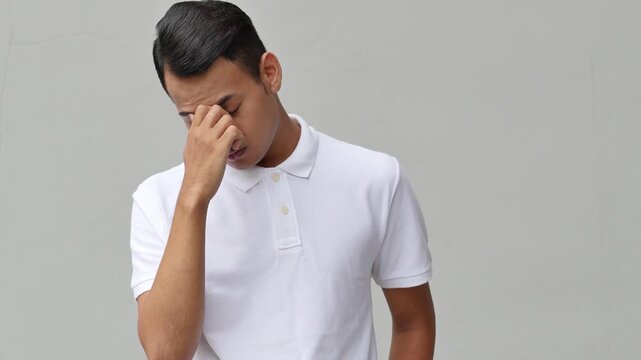 Stressed young adult male with headache, hand pinching nose due to sickness