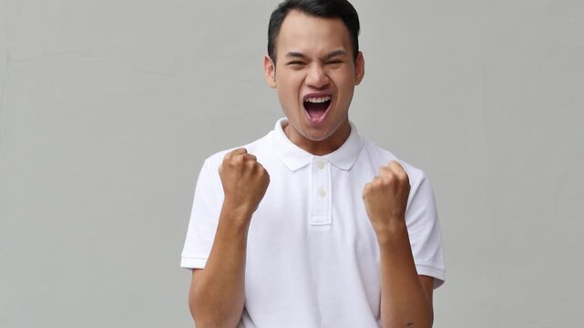 Cheerful Asian man expressing triumph with fist pump and bright smile