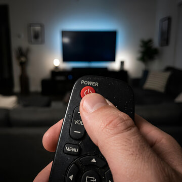 Hand holding TV remote control pressing power button watching television in living room