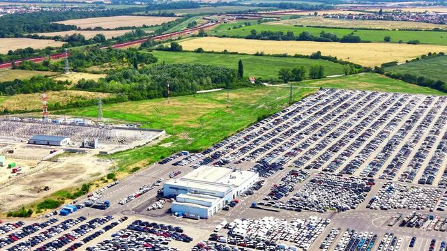 Rural car storage and parking. Many cars are parked in organized rows at a storage facility near a green landscape and fields.