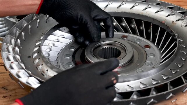 Mechanic hands in black gloves installing thrust bearing into torque converter turbine during automatic transmission rebuild.