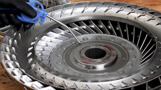 Mechanic hands in gloves cleaning torque converter turbine with air blow gun duster during transmission rebuild.