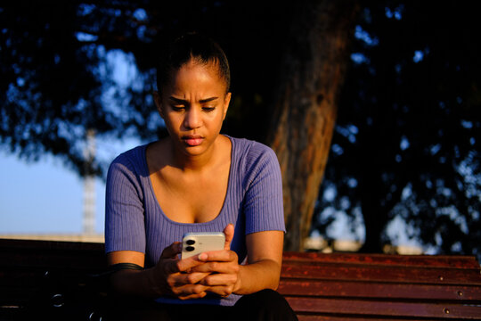Young woman feeling concerned looking at smartphone outdoors