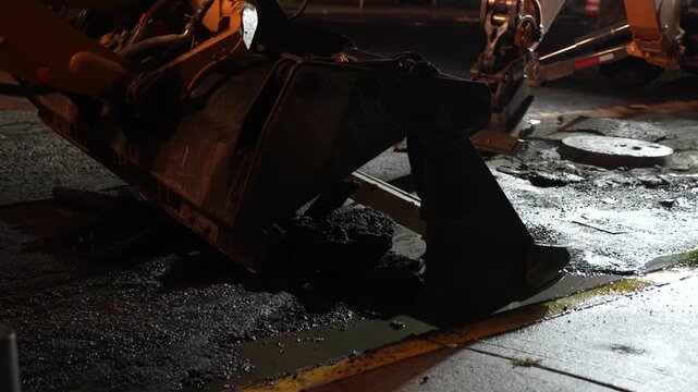 Close-up stock video footage of a heavy industrial excavator hydraulic breaker hammer aggressively breaking up road asphalt on a construction site.
