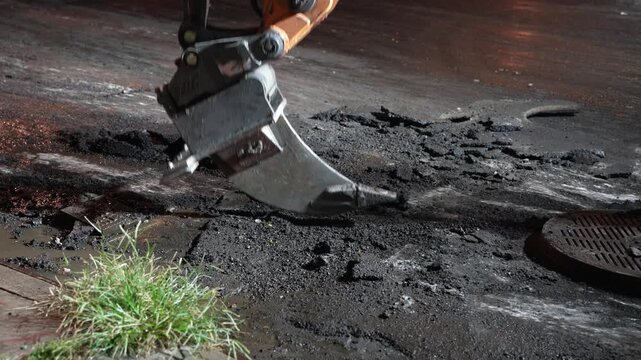 Close-up stock video footage of a heavy industrial excavator hydraulic breaker hammer aggressively breaking up road asphalt on a construction site.
