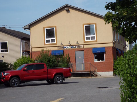 Gatineau, Quebec, Canada &ndash; July 02, 2026: A two-story commercial building with a beige upper level and red brick base features a sign for "Polo Velo" and a parked red pickup truck at  400 Rue Main.