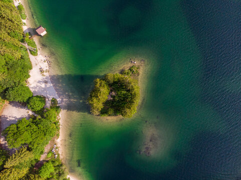 Aerial view of the island in Lago del Predil surrounded by clear turquoise water and lush green forests in Tarvisio, Friuli-Venezia Giulia, Italy.