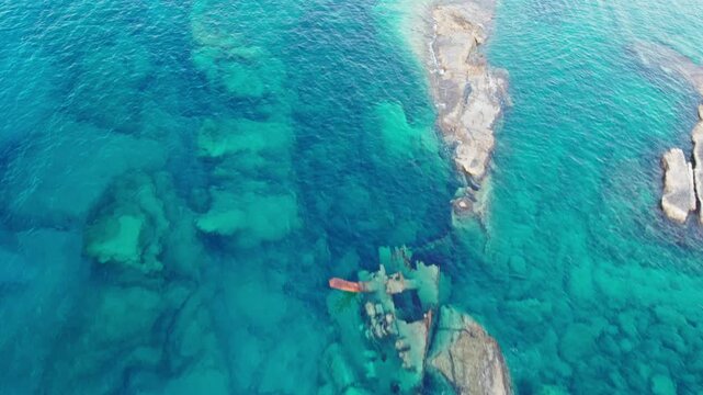 Top-down aerial 4k drone view of a rusting shipwreck blending into the pristine marine ecosystem and crystal-clear waters of Sarakiniko in Milos, Greece.