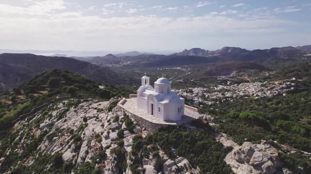 High-angle drone circle of Prophet Elias chapel on Naxos peak, Greece. Whitewashed Cycladic dome against dramatic rocky crags and mountain slopes, Aerial 4k