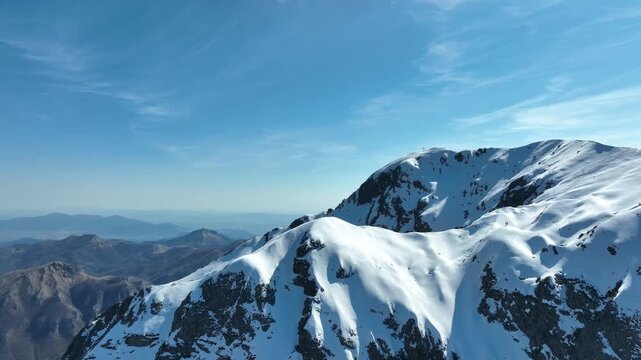 Aerial view of the snow-covered peak of Pania della Croce in the Apuan Alps, with rugged rocky slopes and clear blue sky in Stazzema, Tuscany, Italy.
