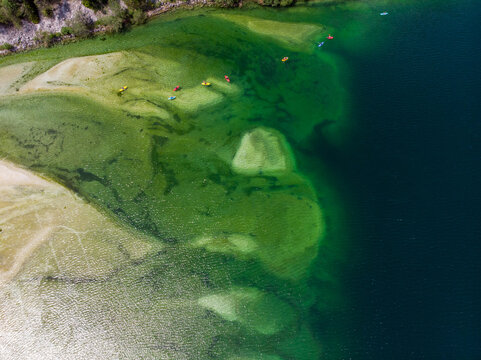 Aerial view of Lago del Predil with colorful kayaks paddling on the clear green water and sandy shallows in Tarvisio, Friuli-Venezia Giulia, Italy.