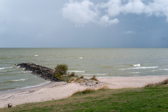 Waves crash on a rocky shore at a beach with gray skies and distant clouds