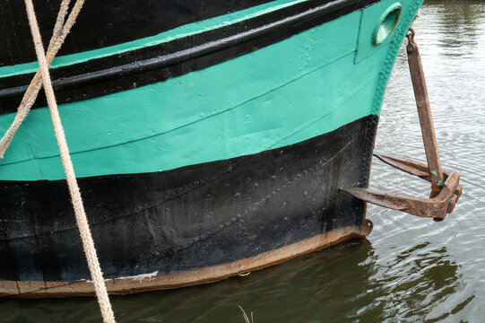 Boat docked by the water with a focus on the hull and anchor during a cloudy day