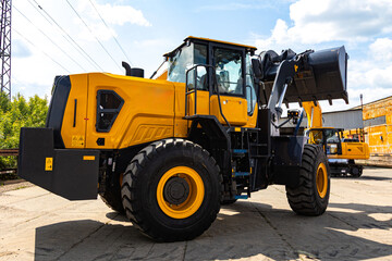 Fototapeta premium Heavy Yellow Wheel Loader with Raised Bucket at Industrial Yard