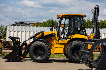 Obraz premium Yellow Backhoe Loader with Front Bucket at Industrial Equipment Yard
