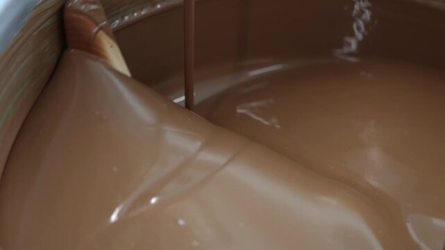 Close-up of smooth melted chocolate being stirred and circulated inside a stainless steel industrial mixing machine at a chocolate factory