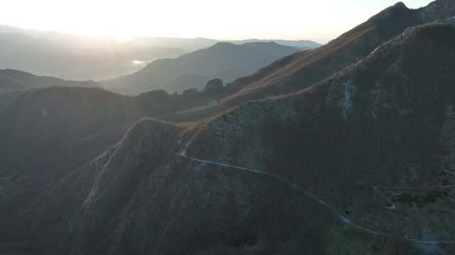 Aerial view of the rugged mountain landscape of Pania della Croce at sunset with a winding road visible along the slopes in Stazzema, Tuscany, Italy.