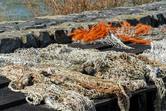 Fishing nets lie on a dock near the water with some orange and white ropes on a sunny day