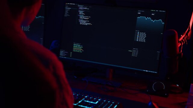 Hacker programming malicious code on a computer in a dark room