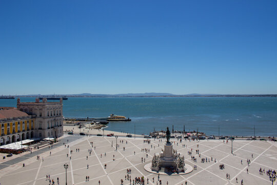 Lisbon, Portugal - 16 August 2017: View of Praca do Comercio with the statue of King Jose I, bustling crowds, and the Tagus River under a clear blue sky.