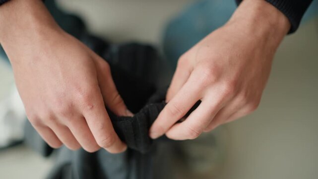 Close up of hands inspecting black fabric texture and weave detail. Hands manipulate material to show softness flexibility in calm indoor setting with neutral background lighting