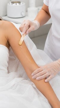 Professional applying wax to a woman's arm in a salon for hair removal.