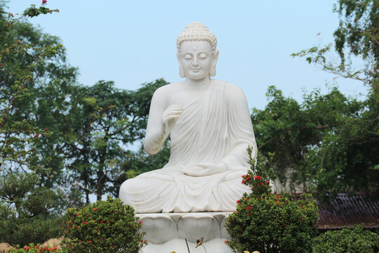 Large white marble Buddha statue in lotus position with Vitarka Mudra gesture, outdoor religious monument at Buddhist temple garden in Hue, Vietnam