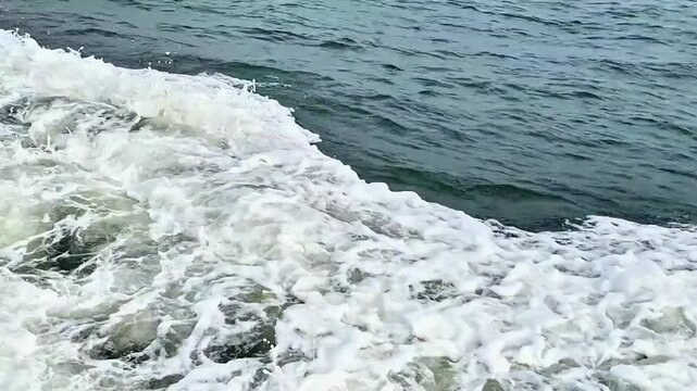 White foam water wake trail created by a fast moving boat engine on deep blue sea surface.