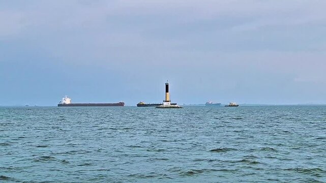 Lighthouse beacon navigation landmark in the middle of the sea with cargo ships passing by.
