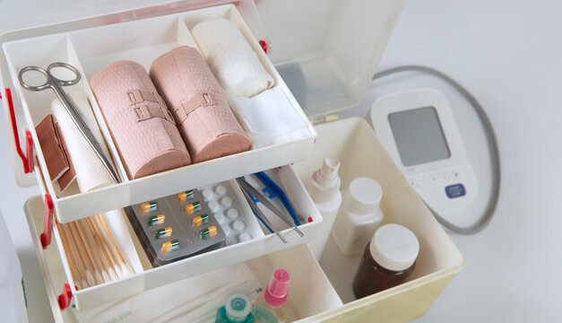 Top view of an organized first aid kit containing bandages, gauze, medical supplies, medicines, face masks, antiseptic spray, and a blood pressure monitor for healthcare, emergency care