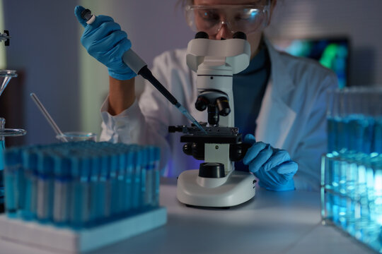 Scientist performing medical research in a laboratory, using a micropipette to transfer liquid onto a microscope slide for advanced biotechnology analysis and experiment